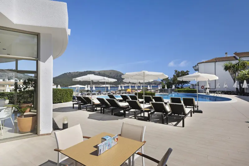 Transats blancs disposés autour d'une piscine ensoleillée avec vue sur la mer.