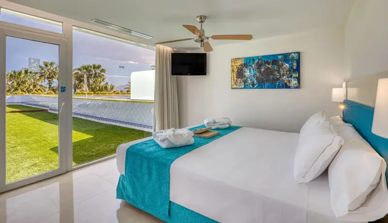 Une chambre lumineuse avec un grand lit et vue sur un jardin verdoyant.