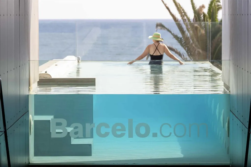 Une personne se tient dans une piscine à débordement avec vue sur la mer.