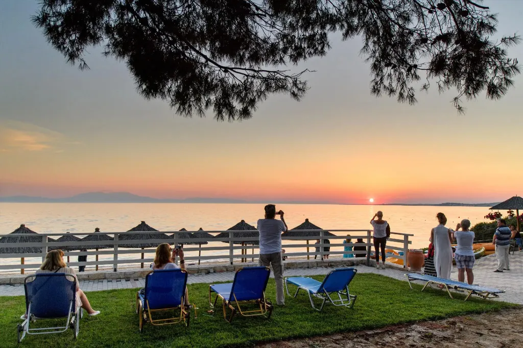 Des personnes se détendent sur une pelouse face à la mer au coucher du soleil.