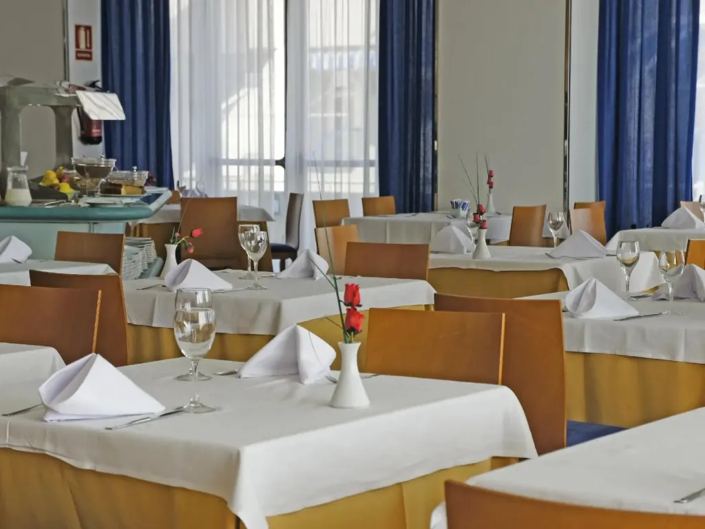 Une salle lumineuse est aménagée avec des tables dressées pour un repas.