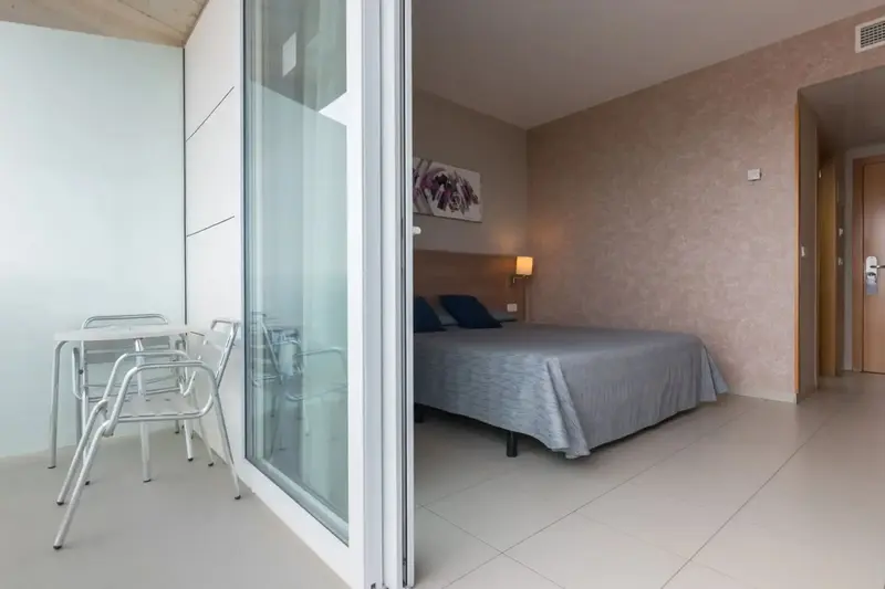 Une chambre lumineuse s'ouvre sur un balcon avec table et chaises.