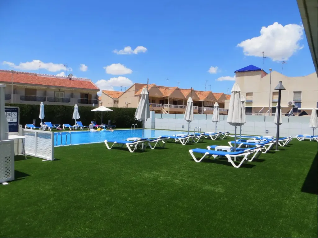 Transats bleus alignés sur une pelouse verte au bord d'une piscine ensoleillée.