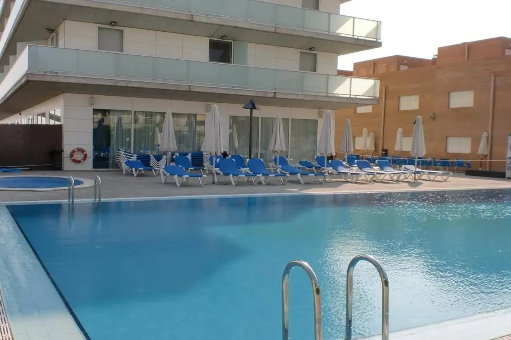 Une piscine bleue bordée de transats blancs et bleus, devant un bâtiment moderne.