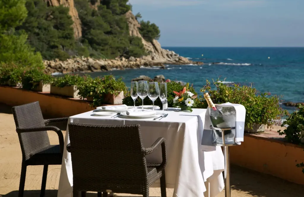 Table dressée en extérieur avec vue sur la mer et la côte rocheuse.