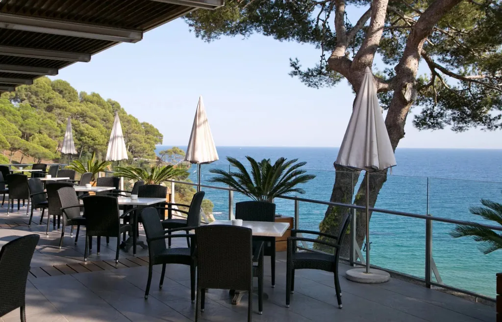 Terrasse ombragée avec tables et chaises donnant sur la mer.