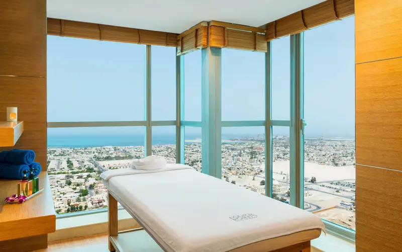 Table de massage blanche dans une pièce lumineuse avec une vue panoramique sur la ville et la mer.
