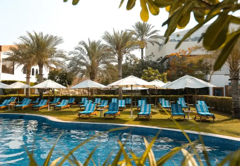Transats bleus et parasols blancs bordent une piscine turquoise au milieu d'une végétation luxuriante.
