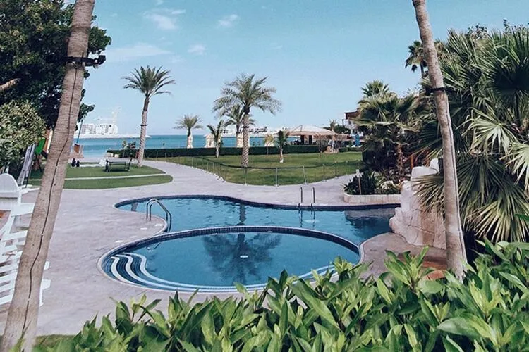 Piscines d'un complexe hôtelier avec végétation luxuriante et vue sur la mer.