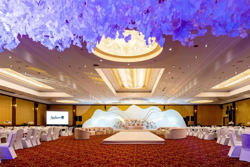 Une grande salle de réception est aménagée avec des tables et des chaises pour un événement.