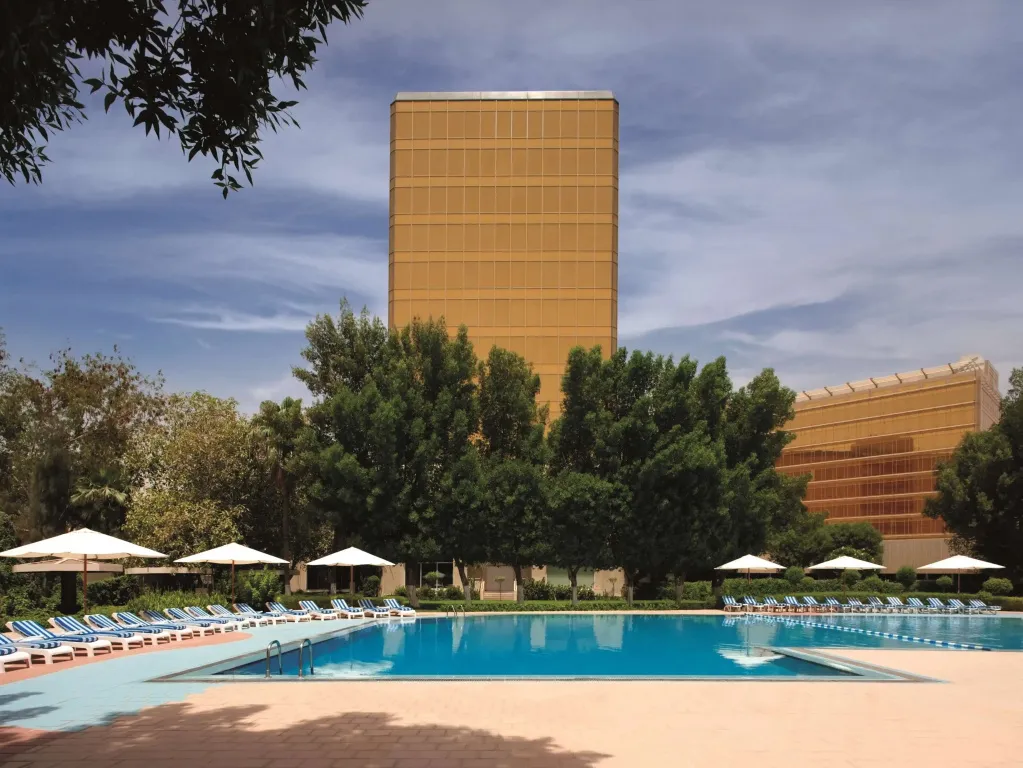 Une grande piscine bordée de transats devant un bâtiment imposant.