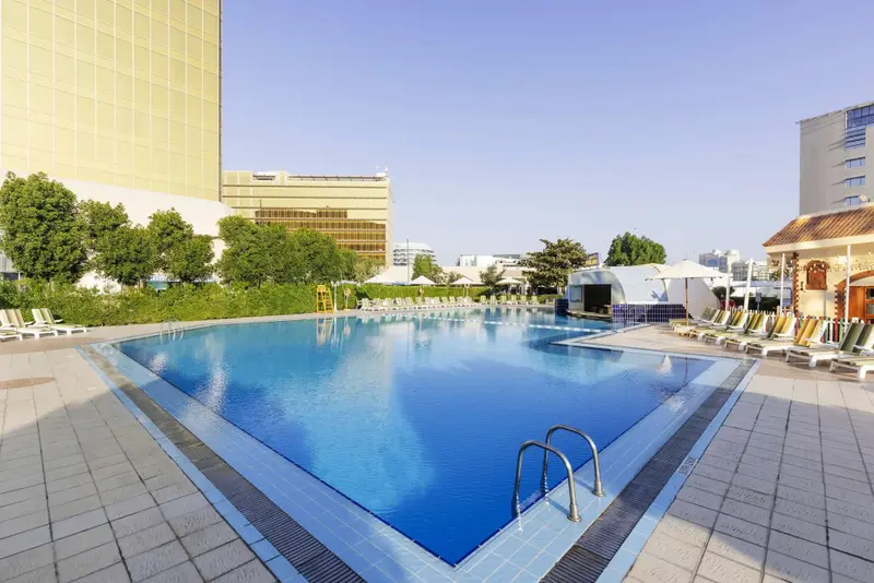 Une piscine rectangulaire bordée de chaises longues sous un ciel bleu.
