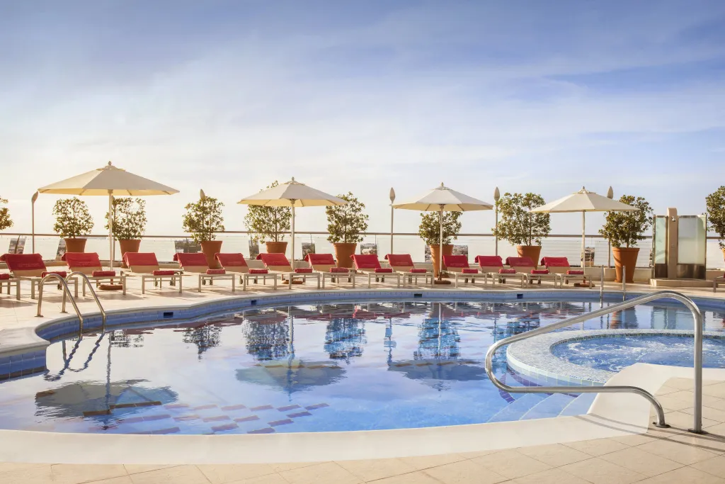 Piscine extérieure avec transats rouges et parasols blancs.