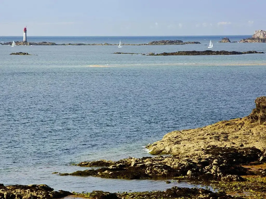 Vue sur la mer avec un phare et des voiliers à l'horizon.