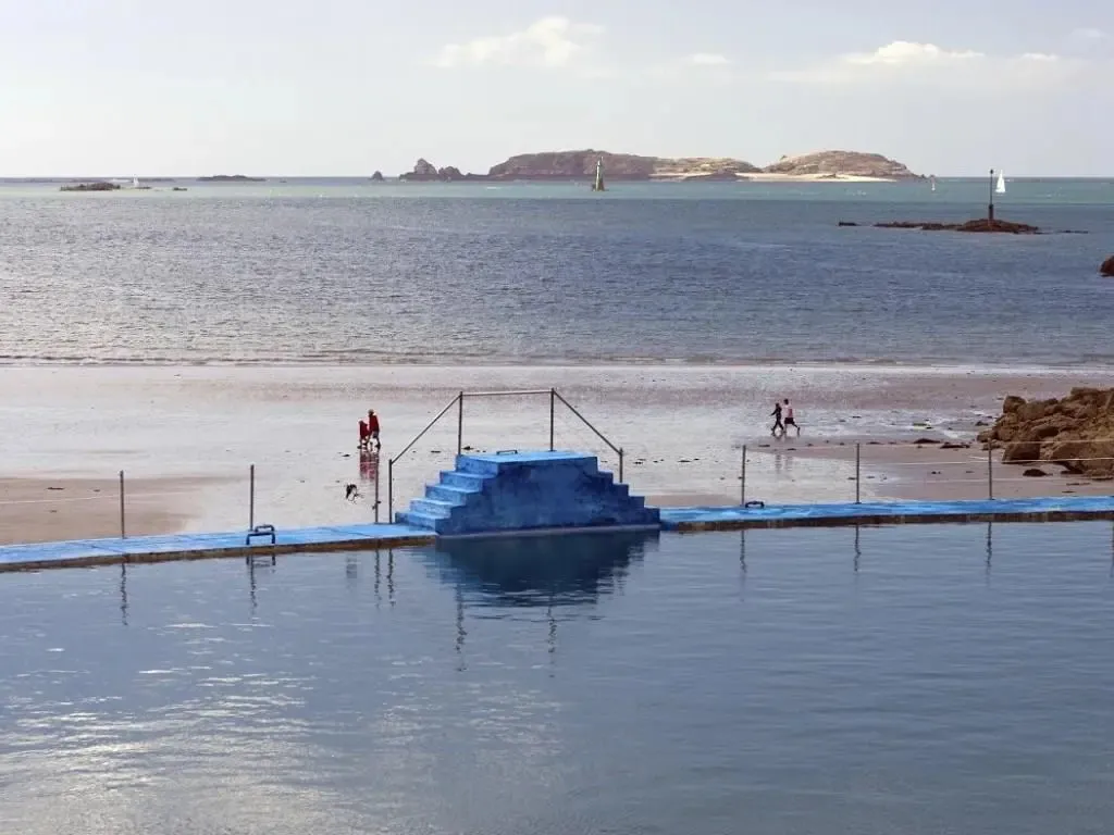Une piscine bleue rectangulaire avec des marches et une vue sur la mer.