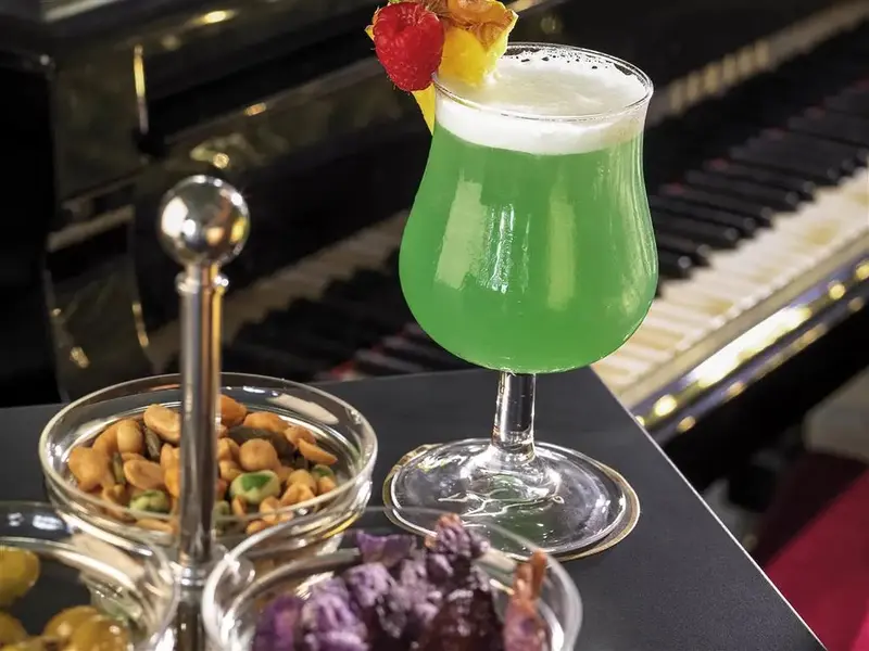 Un cocktail vert est servi avec des amuse-gueules devant un piano à queue.