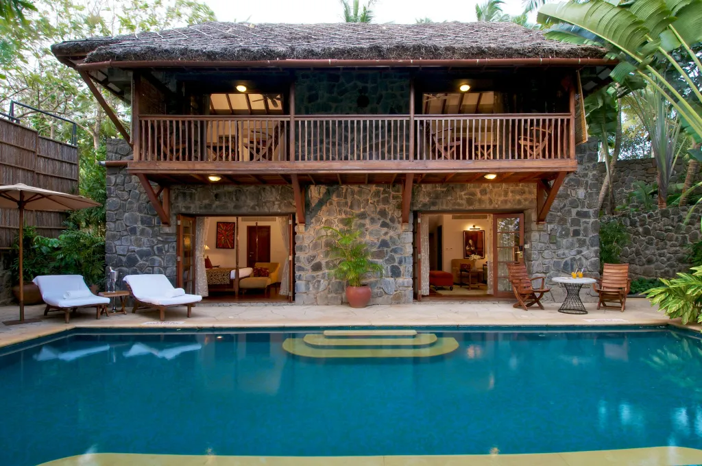 Bâtiment en pierre avec des ouvertures sur une piscine et une végétation luxuriante.