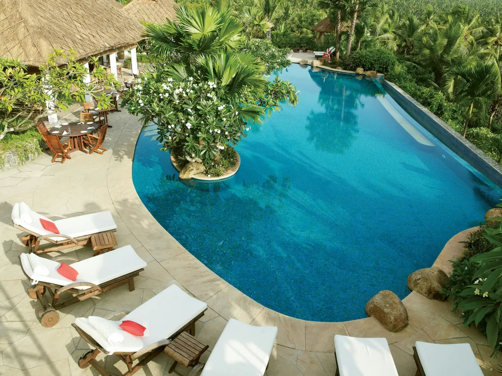 Piscine turquoise entourée de chaises longues et de végétation luxuriante.
