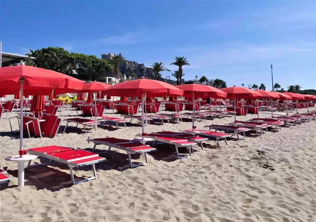 Transats rouges alignés sur une plage de sable fin sous des parasols.