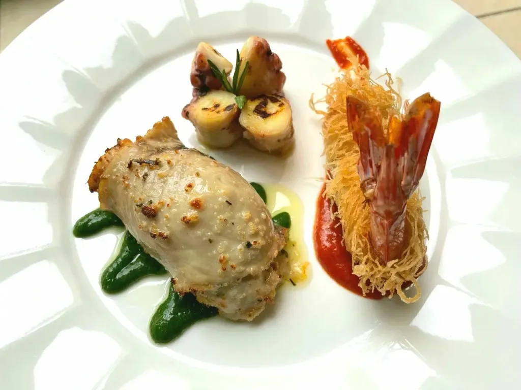 Assiette gastronomique composée de fruits de mer et de sauces colorées.