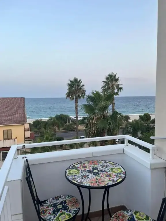 Une terrasse avec une table et des chaises offre une vue sur la mer et la végétation.