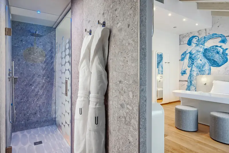 Une douche à l'italienne moderne s'ouvre sur une chambre décorée d'une fresque murale.