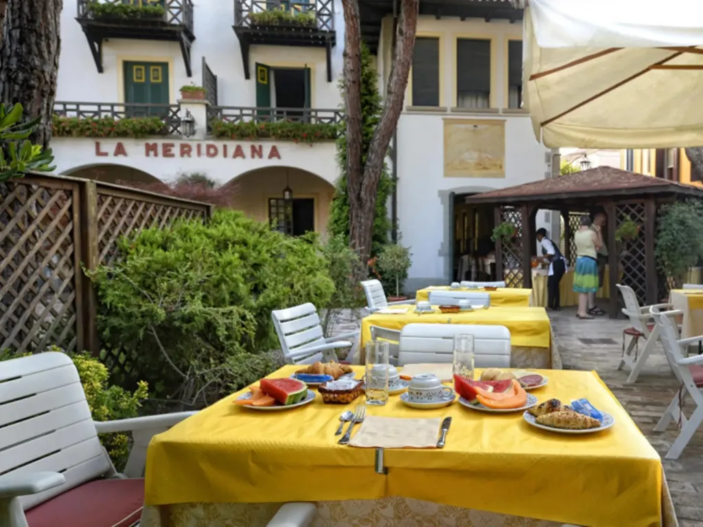 Tables colorées dressées pour un repas en extérieur dans une cour ombragée.