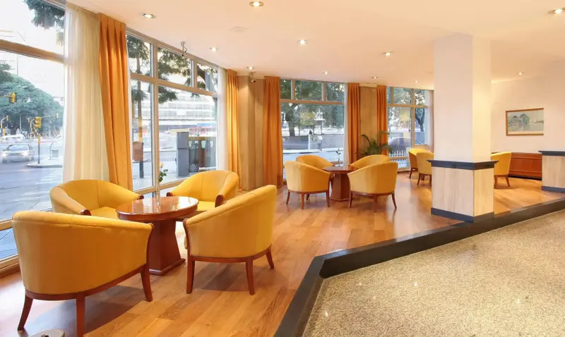 Espace de détente lumineux avec des fauteuils et des tables basses près de grandes fenêtres.