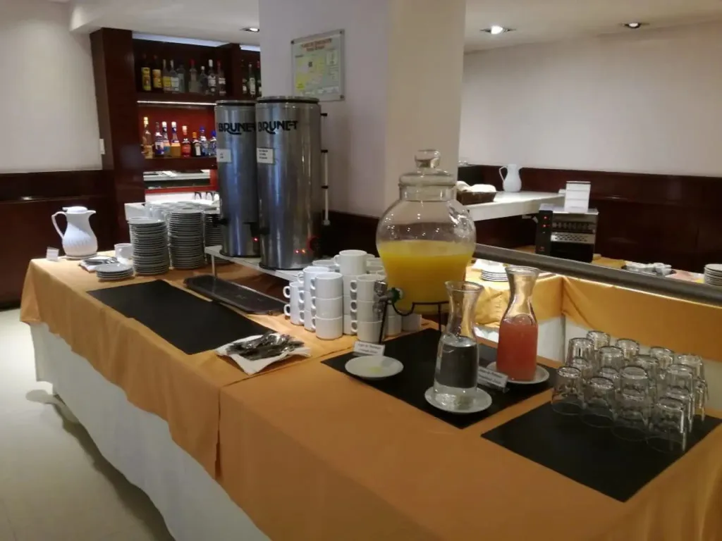 Un buffet propose des boissons et de la vaisselle sur une table recouverte d'une nappe.