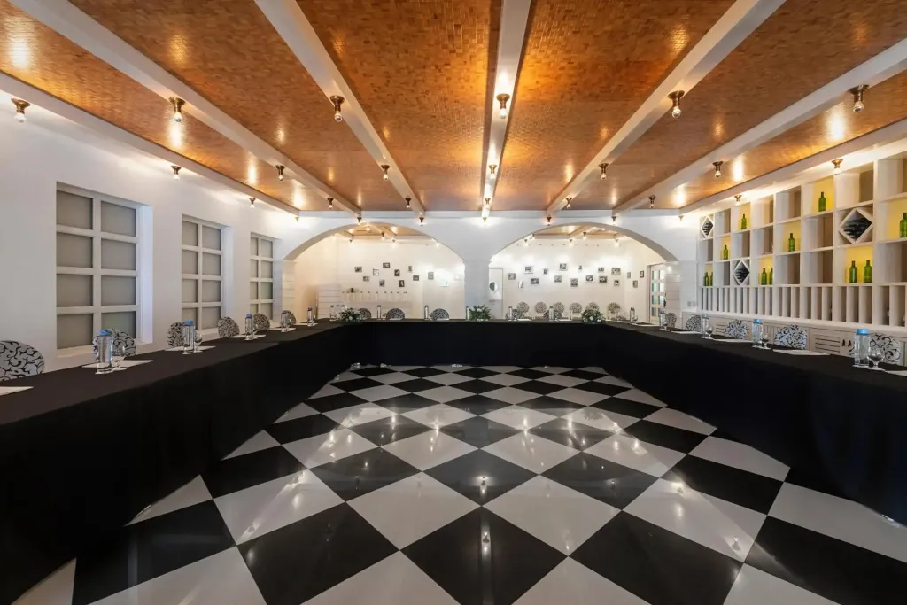 Une salle aux murs blancs et au sol à carreaux noirs et blancs est aménagée avec des tables dressées.