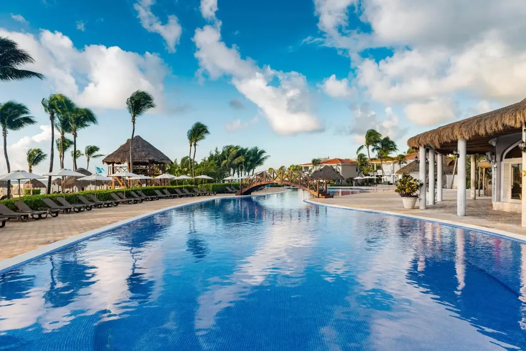 Une grande piscine rectangulaire bordée de transats sous des parasols.