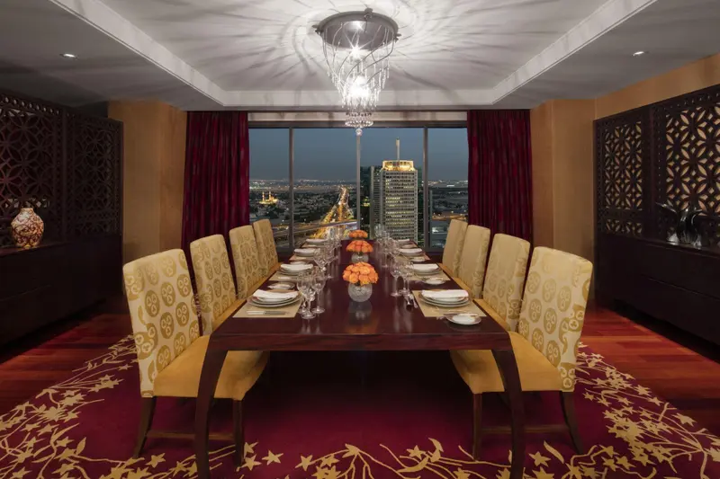 Une longue table de repas est dressée dans une salle lumineuse avec vue sur la ville.