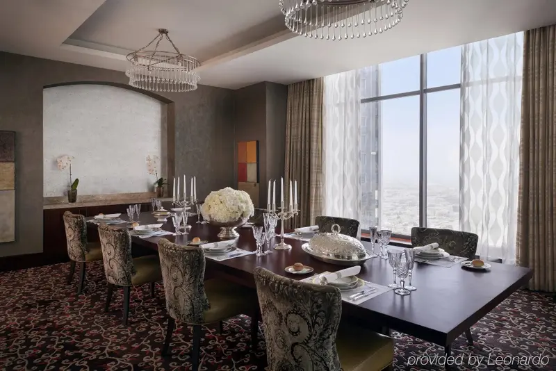 Une longue table de repas est dressée dans une salle lumineuse avec de grandes fenêtres.