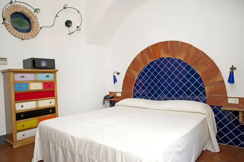 Une chambre lumineuse avec un lit recouvert d'un drap blanc et une commode colorée.
