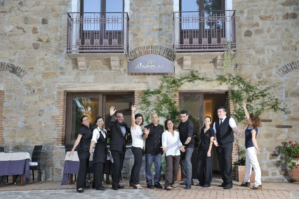 Groupe de personnes souriantes devant un bâtiment en pierre avec des balcons fleuris.