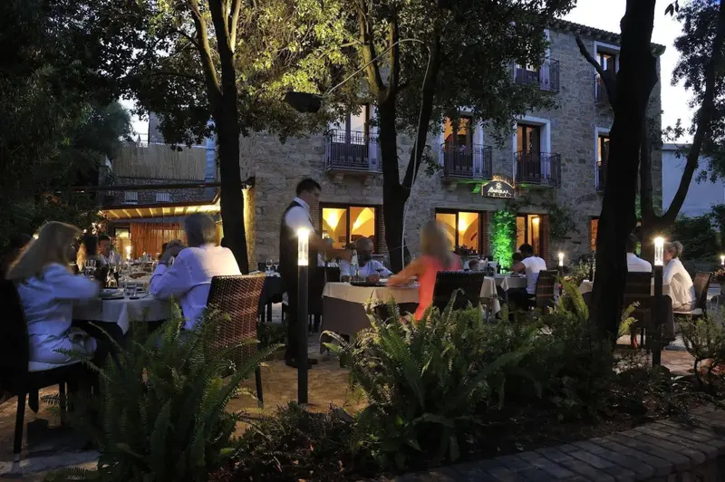 Une terrasse illuminée accueille des convives autour de tables nappées.