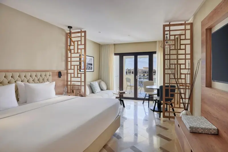 Une chambre lumineuse avec un grand lit et un coin repas près d'une baie vitrée.
