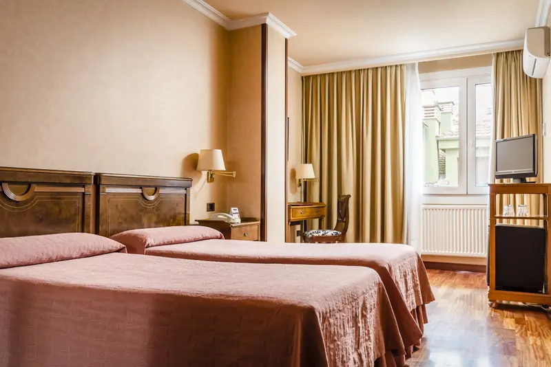 Une chambre d'hôtel lumineuse avec deux lits simples et un bureau près de la fenêtre.