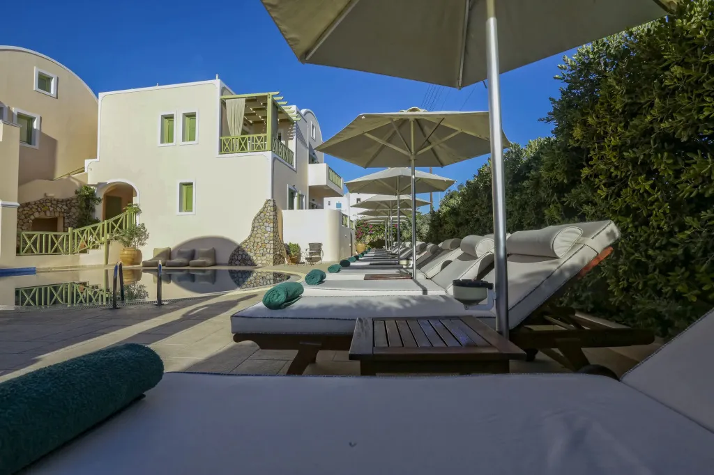 Transats blancs alignés sous des parasols près d'une piscine ensoleillée.