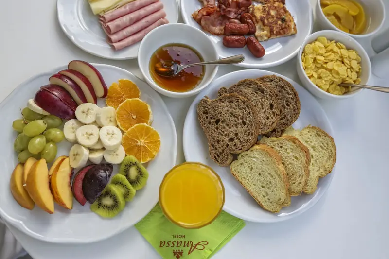 Assortiment de fruits frais, charcuterie, céréales et pain sur une table blanche.