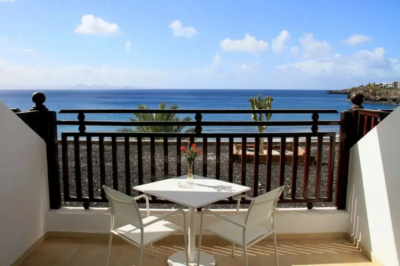 Une table et deux chaises blanches sont disposées sur un balcon avec vue sur la mer.