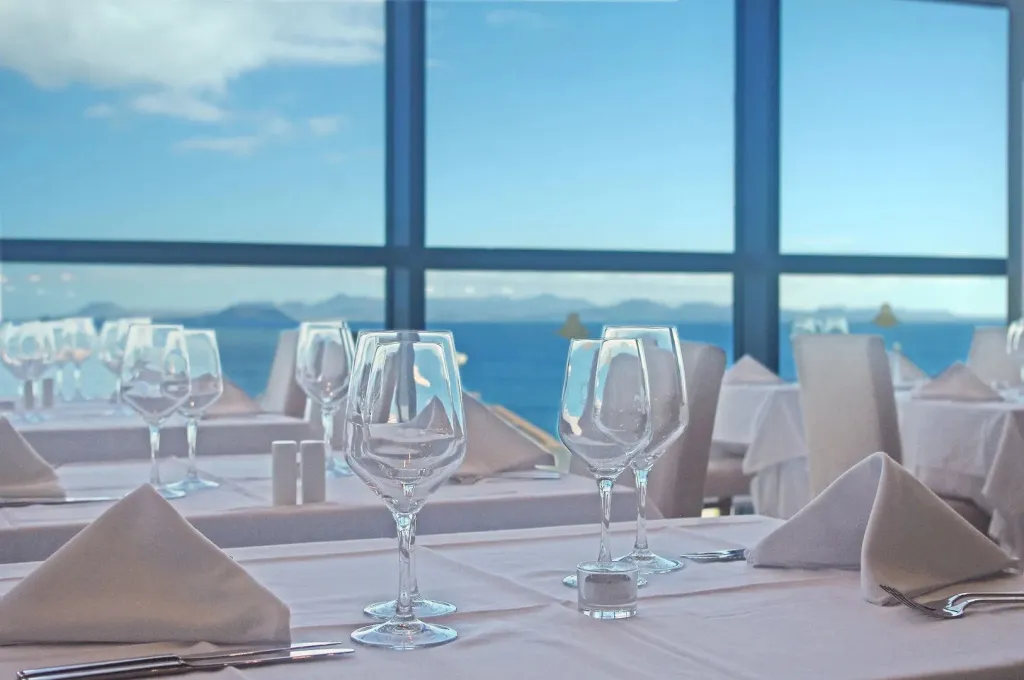 Une table est dressée devant une grande baie vitrée donnant sur la mer.