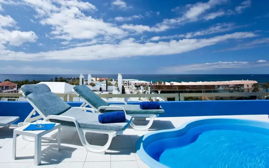 Transats bleus et piscine sur une terrasse ensoleillée avec vue sur la mer.