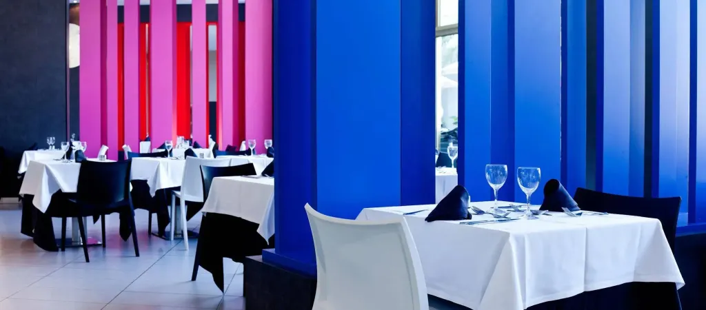 Une salle lumineuse avec des tables dressées pour un repas.