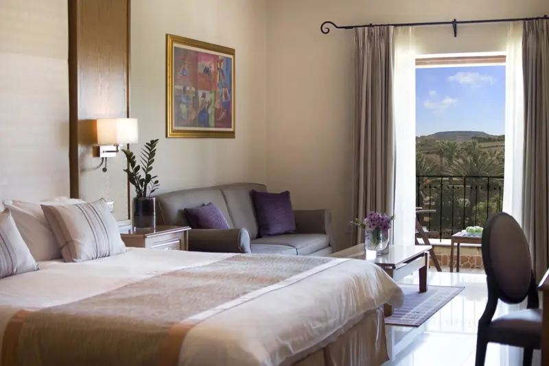 Une chambre lumineuse avec un grand lit et un coin salon donnant sur une vue verdoyante.