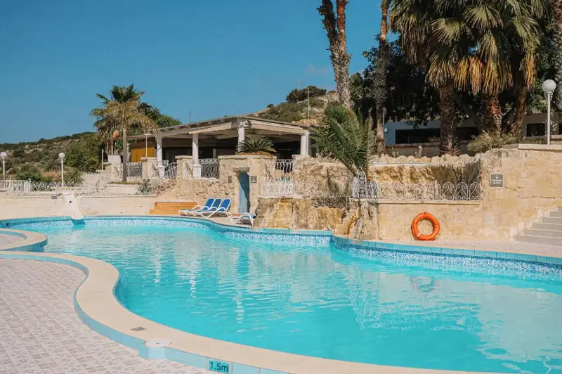 Piscine turquoise bordée d'une terrasse ensoleillée avec des transats.