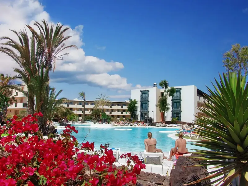 Une piscine turquoise bordée de chaises longues et de végétation luxuriante.