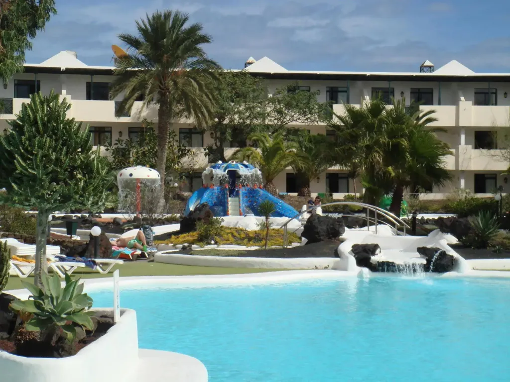 Une piscine turquoise avec une cascade rocheuse et des transats.