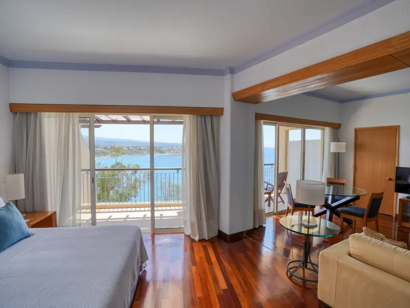 Une chambre lumineuse avec un lit et un espace repas donnant sur une vue mer.