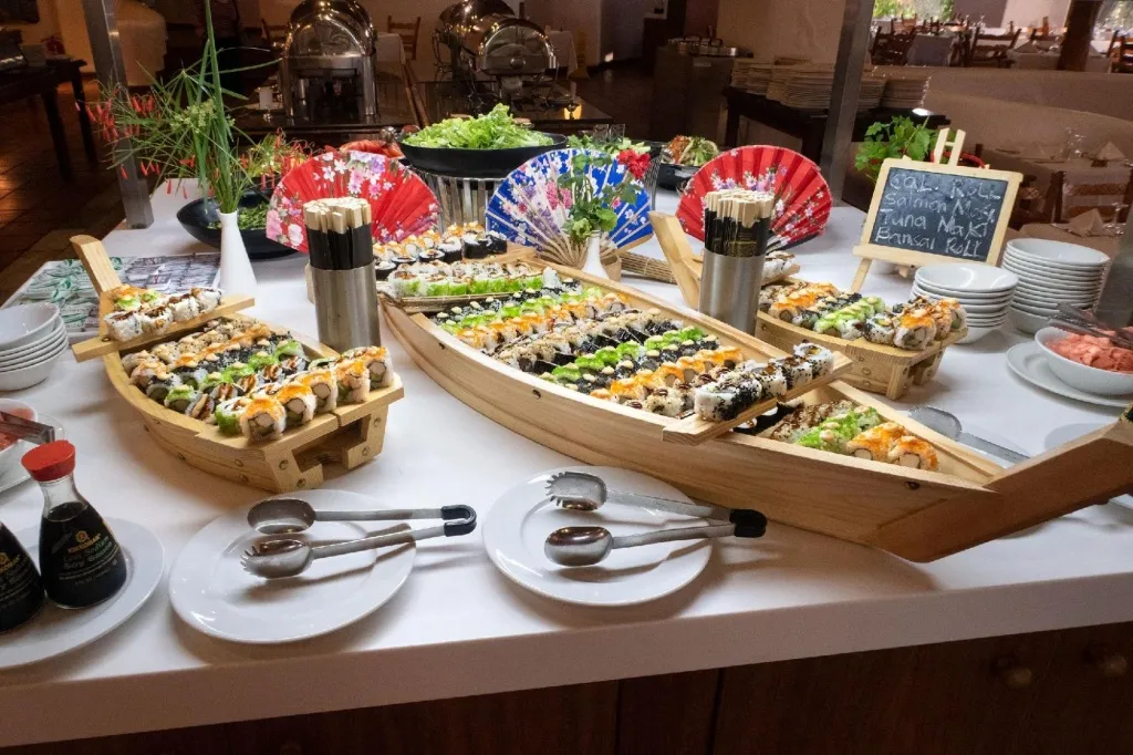 Présentation de sushis variés sur un buffet décoré de bateaux en bois et d'éventails.